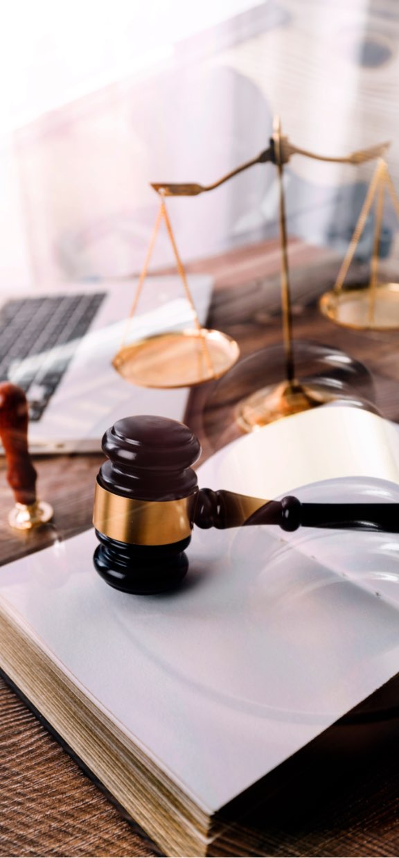 The gavel of a criminal defense lawyer and a set of scales sit on an open book ontop of a desk..